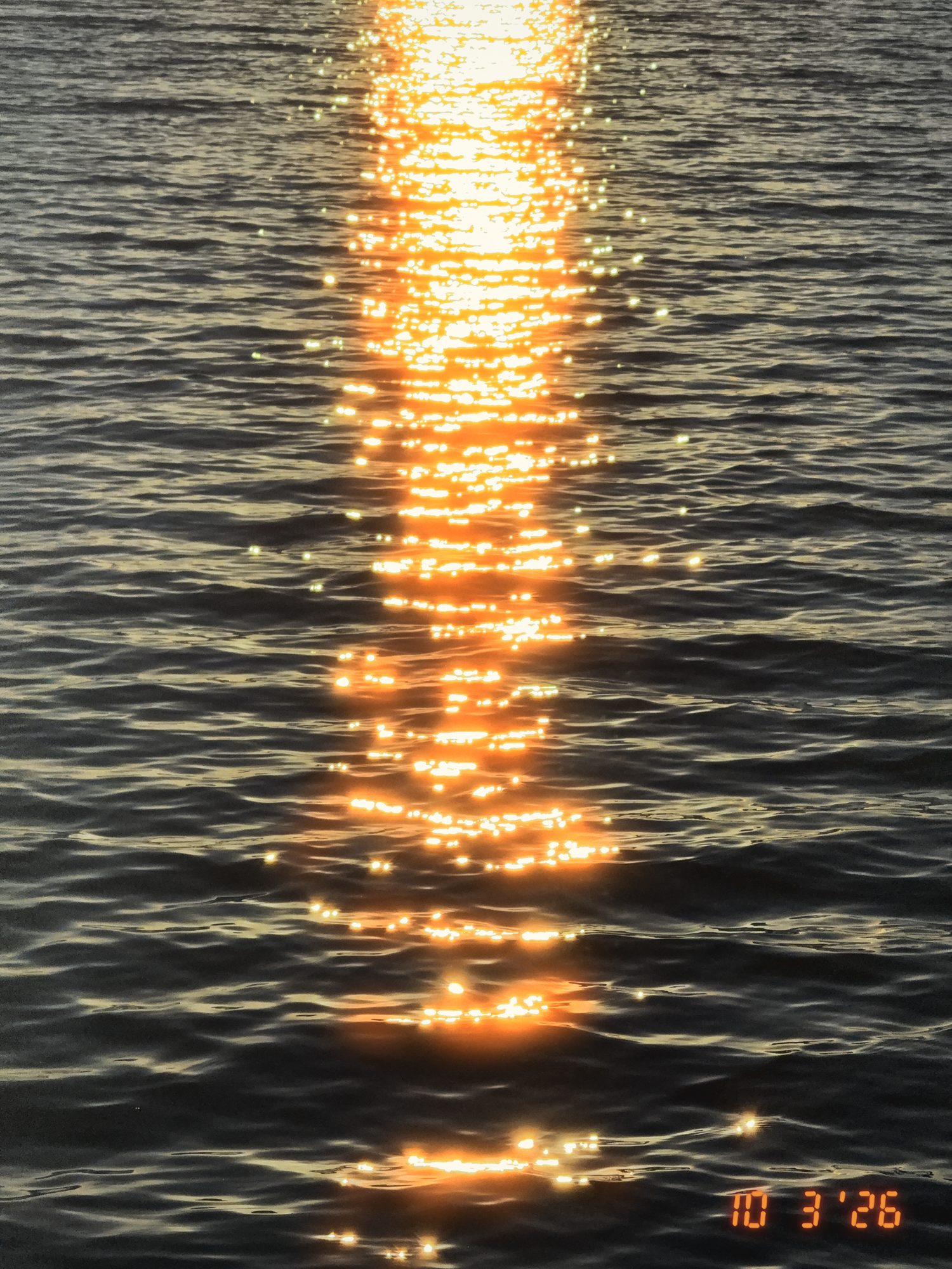 Low sun laying a column of glittering orange light across dark, rippled lake water